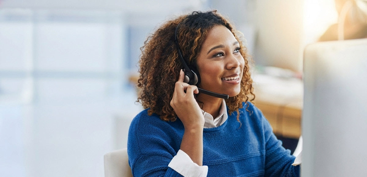 A smiling woman with curly brown hair wearing a blue shirt and call center headphones. 